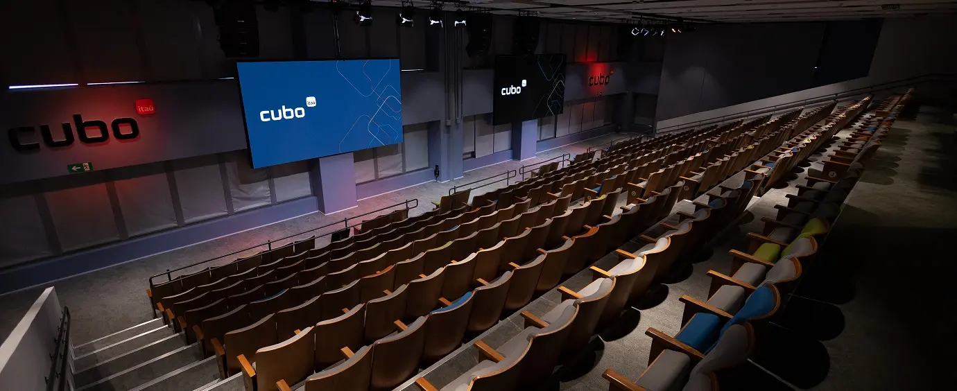 Auditório do Cubo Itaú, com a tela do palco ao fundo e as poltronas em arquibancada